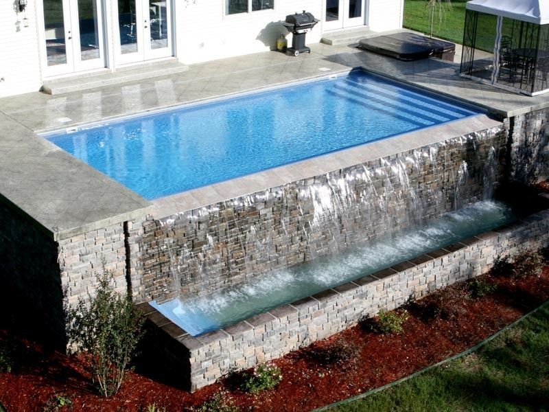 Rectangular backyard pool with a rock waterfall spilling into a lower basin, surrounded by a patio