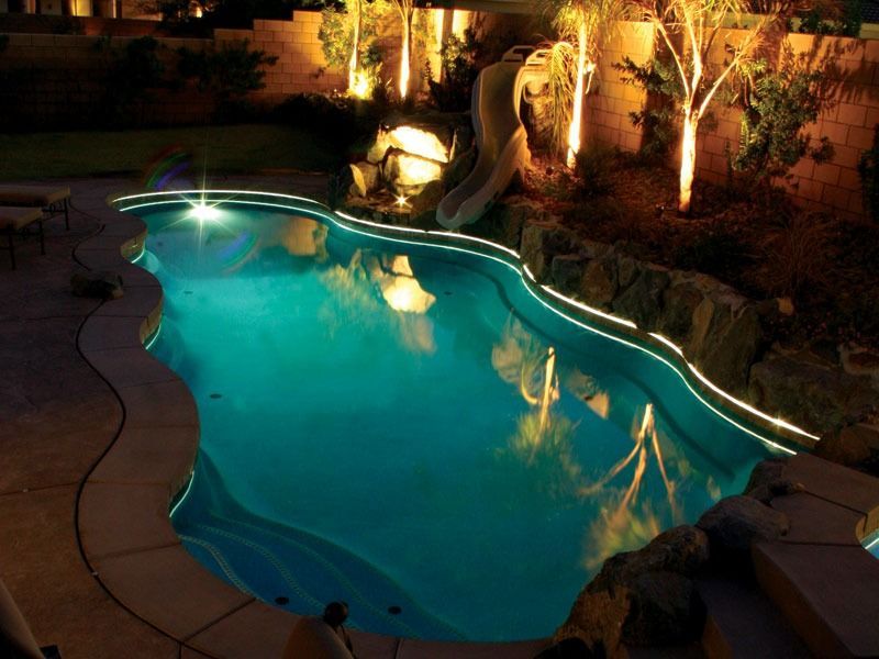 Illuminated backyard swimming pool at night with turquoise water and surrounding patio lights