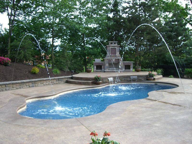 Backyard pool with a stone fountain and arcing water jets, surrounded by trees and a patio.