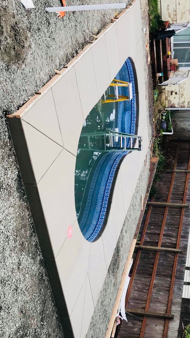 Outdoor swimming pool under construction, with blue liner, concrete deck, and surrounding fencing.