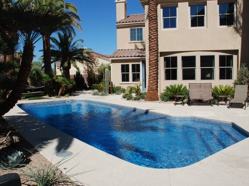 Backyard swimming pool beside a beige house with palm trees and lounge chairs