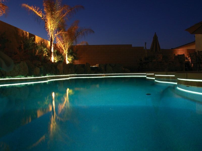 Illuminated backyard pool at dusk with palm trees and glowing water reflections