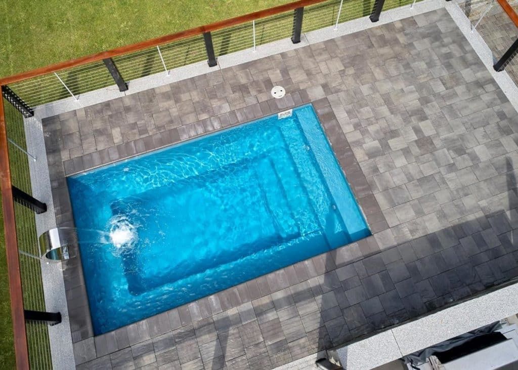 Rectangular blue swimming pool surrounded by gray stone patio, viewed from above