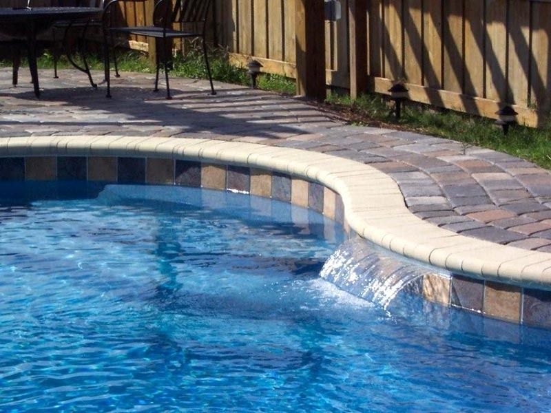 Backyard swimming pool with blue water, tiled edge, and a small waterfall spillway