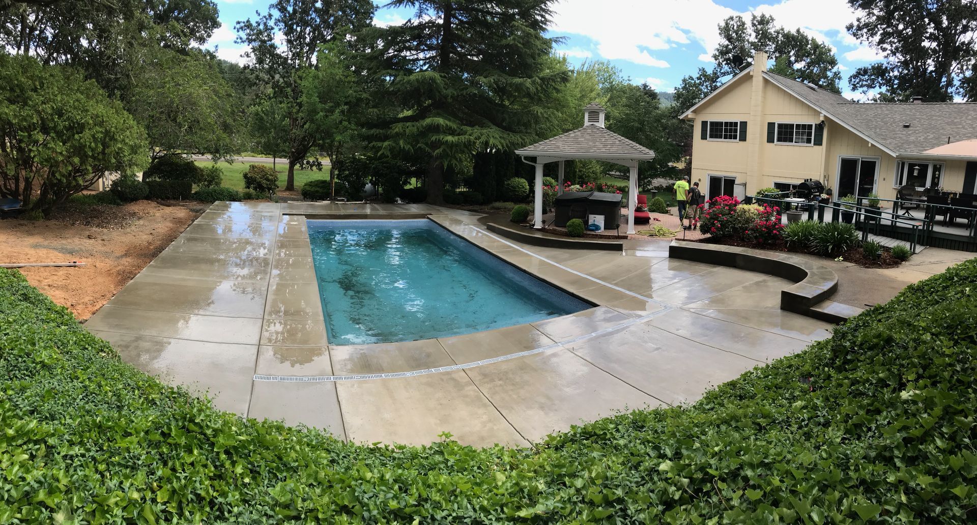 Outdoor swimming pool with surrounding patio, gazebo, and building in a landscaped courtyard.