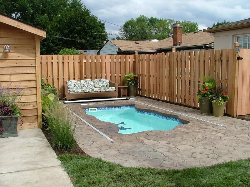 Small backyard patio with an above-ground pool, wooden fence, potted plants, and a shed beside a concrete walkway