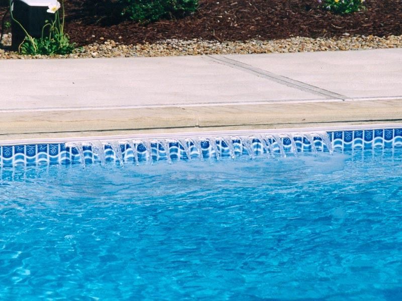 Blue swimming pool beside a beige concrete deck and landscaped edge