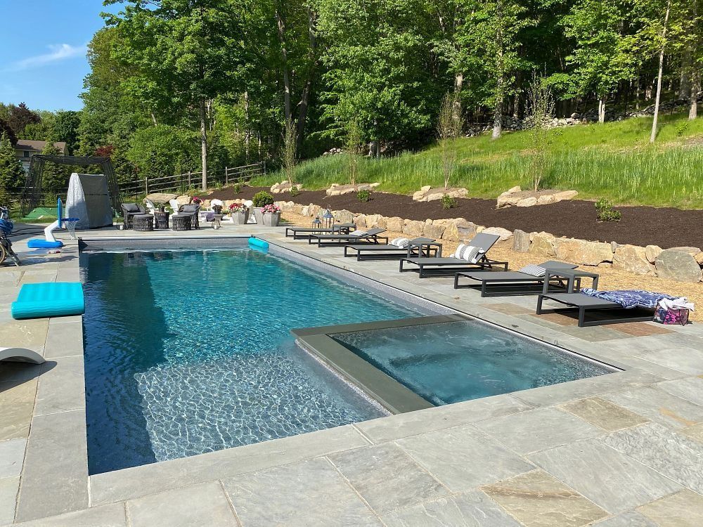 Modern outdoor pool with lounge chairs, turquoise water, and green hillside trees