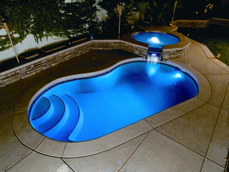 Blue-lit backyard pool with attached spa at night