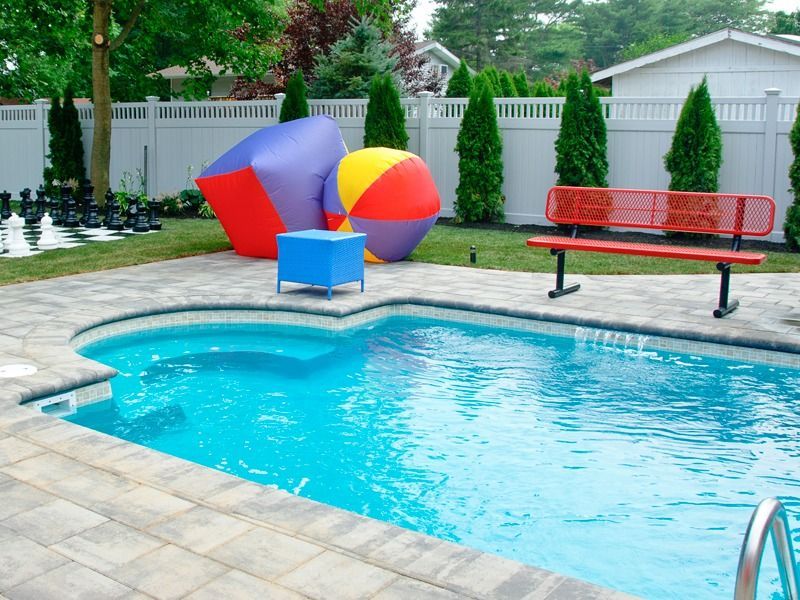 Backyard pool with colorful beach balls, red bench, blue table, and white fence