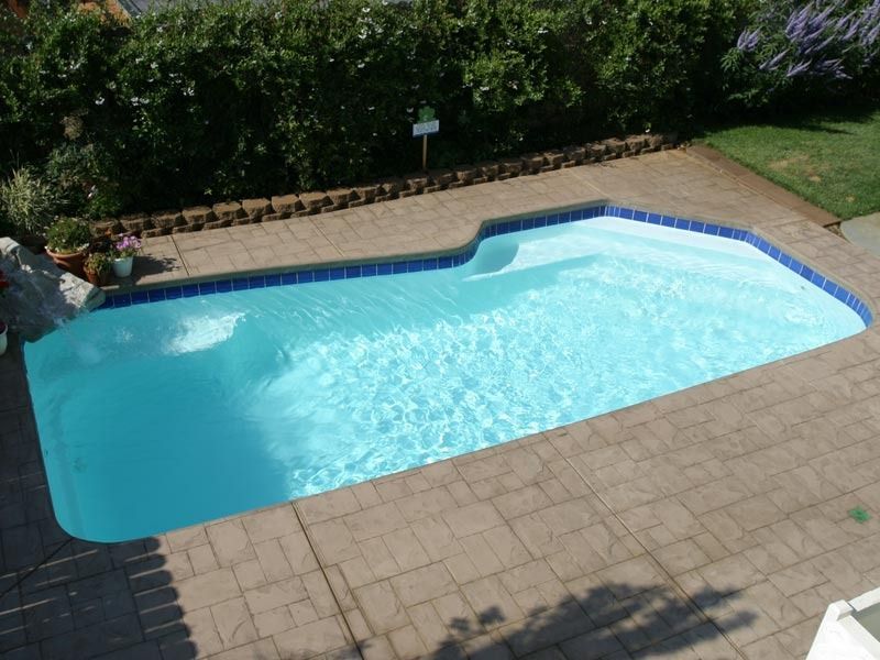 Backyard swimming pool with light blue water, tan pavers, and surrounding greenery