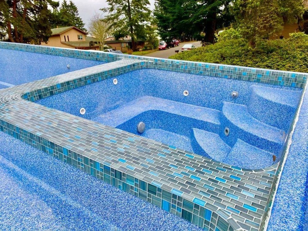 Empty blue mosaic swimming pool with built-in benches in a landscaped backyard