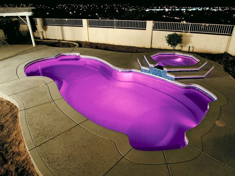 Backyard pool glowing purple at night with a connected spa and lounge chairs nearby
