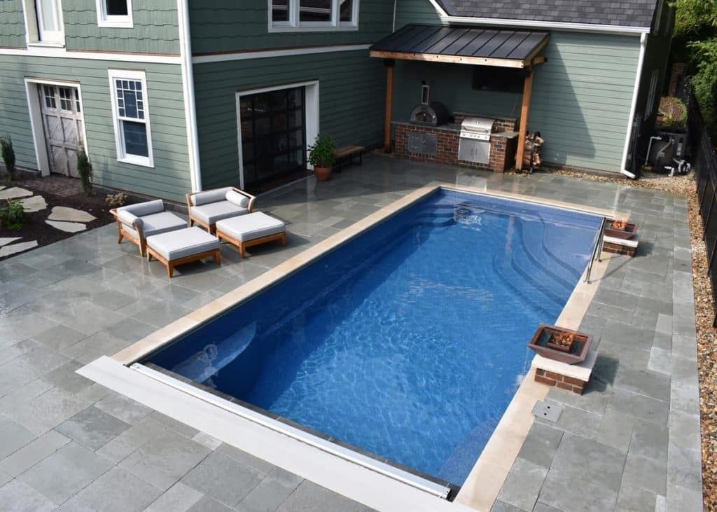 Backyard pool with blue water, lounge chairs, and a covered patio beside a house