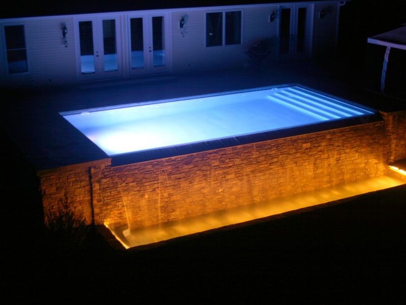 Illuminated rooftop pool at night with blue water and warm orange underlighting