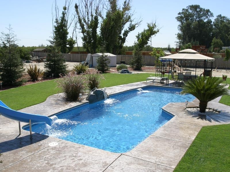 Backyard swimming pool with blue water, patio, gazebo, and landscaped lawn under clear skies
