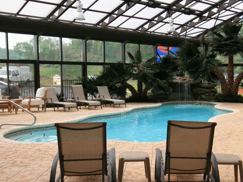 Indoor pool area with turquoise water, lounge chairs, and large windows overlooking greenery