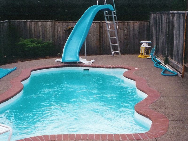 Backyard swimming pool with a blue slide, ladder, and fence surrounding it