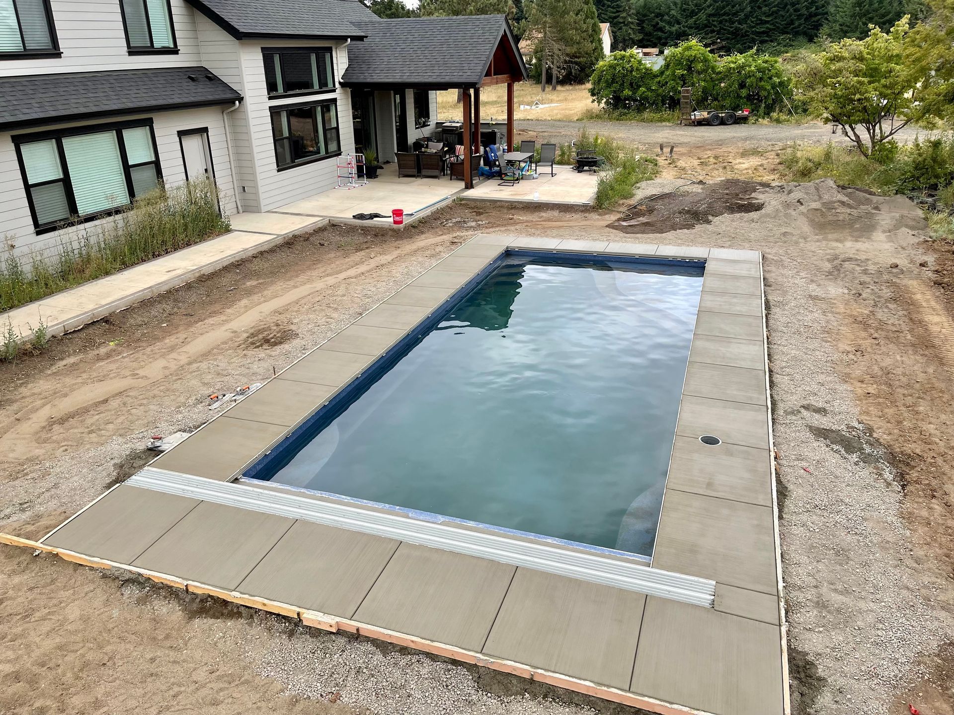 Rectangular backyard pool beside a house, with stone coping and a gravel patio.