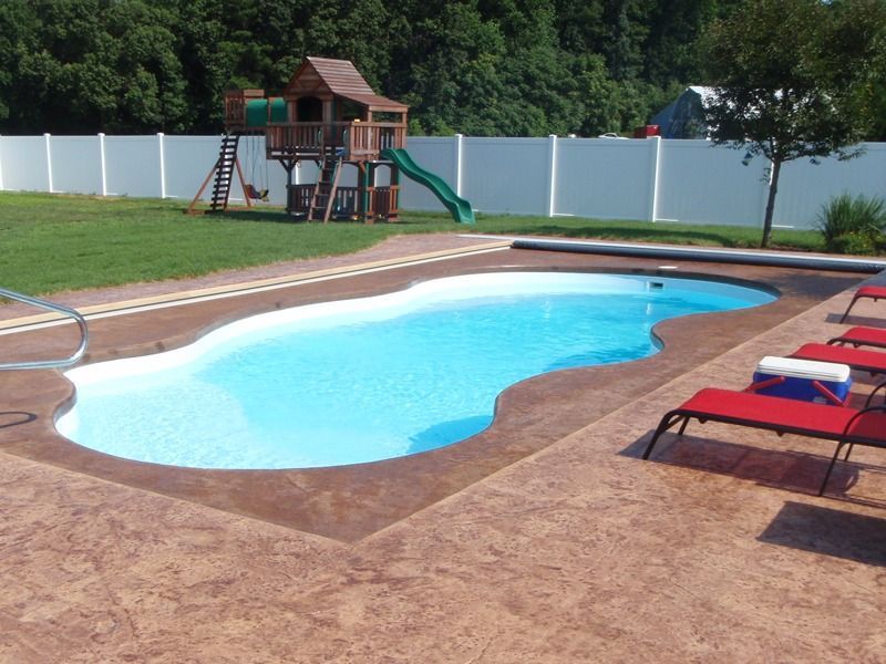 Backyard pool with red lounge chairs, playground, and white fence under a clear sky