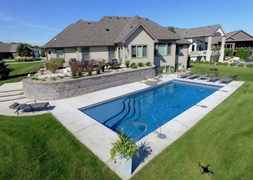 Backyard with a rectangular blue swimming pool beside a stone patio and a modern house