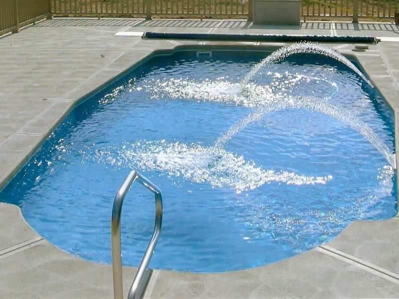 Backyard swimming pool with water spraying in from a fountain and a metal handrail in the foreground