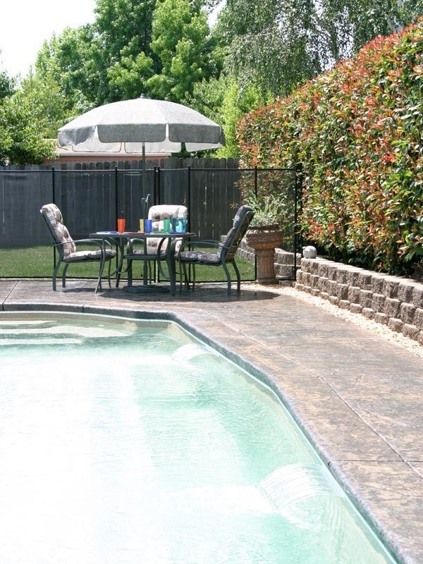 Backyard pool with patio table, chairs, umbrella, and privacy fence along the side