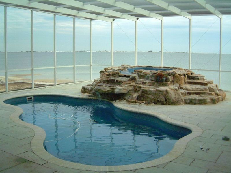 Indoor pool beside a stone spa, with ocean views through large glass walls
