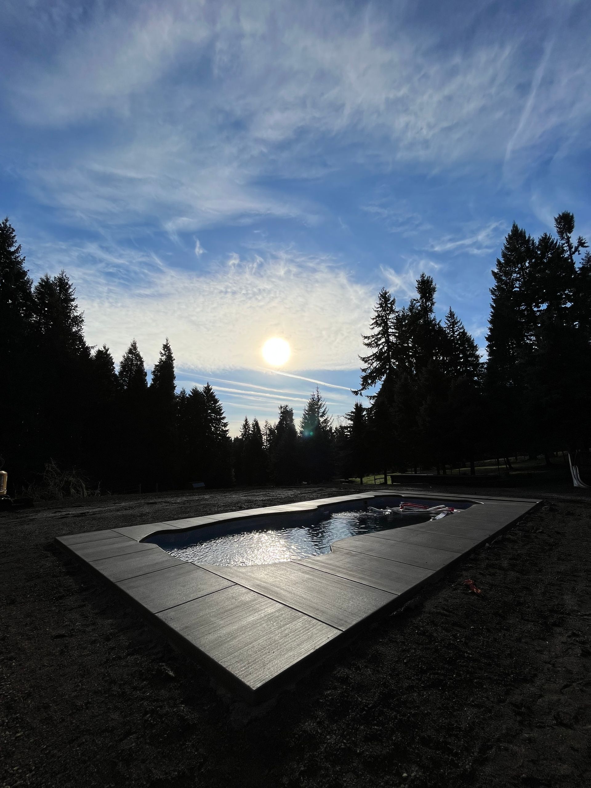 Sunrise over a reflecting pool in a dark forest, with a bright sky and silhouetted trees.
