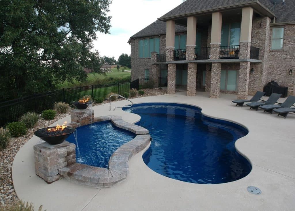 Backyard patio with a blue swimming pool, spa, stone fire pit, and a house with balcony overlooking the water