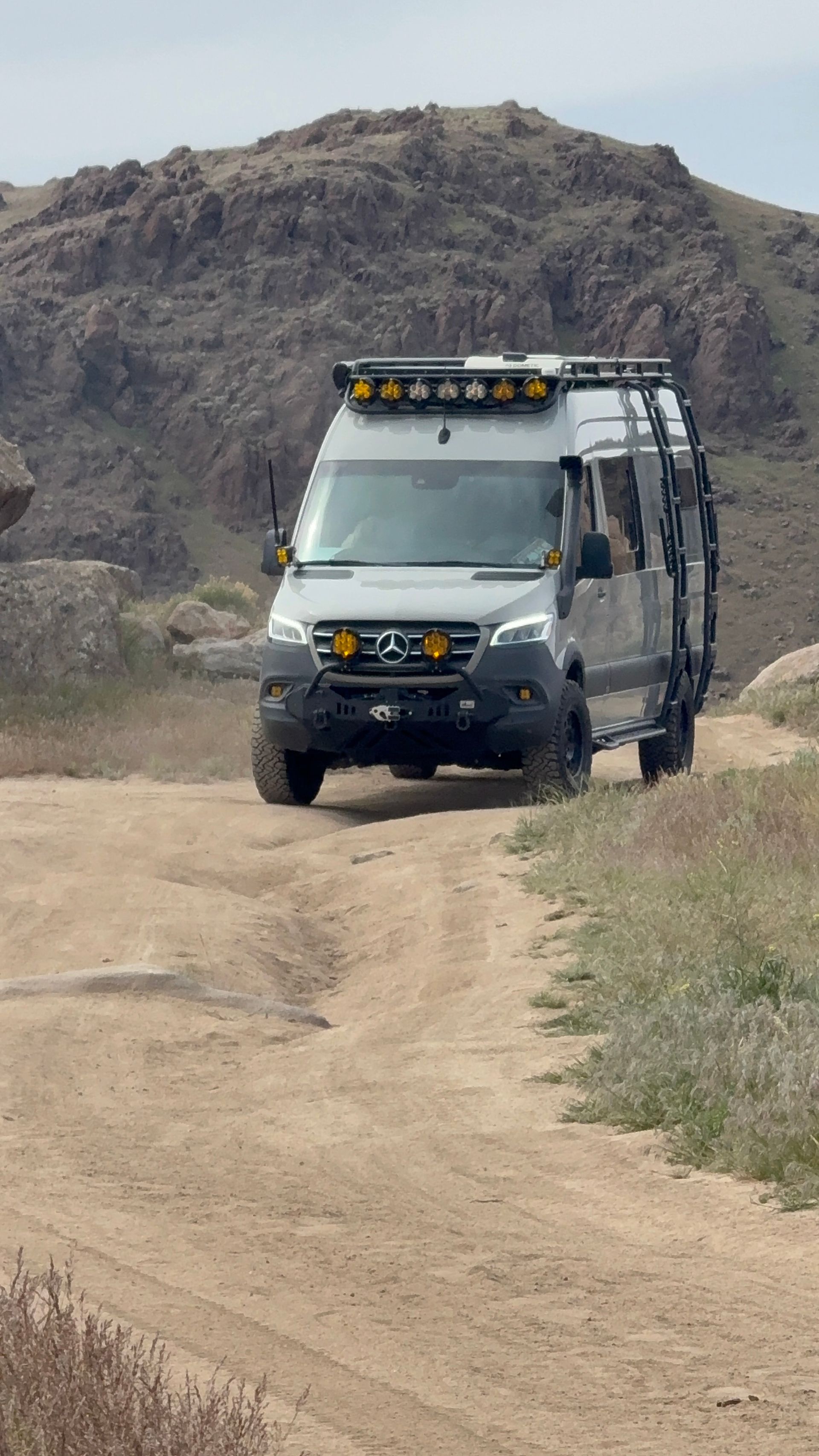 White off-road van on a dirt path in a rocky, barren landscape.