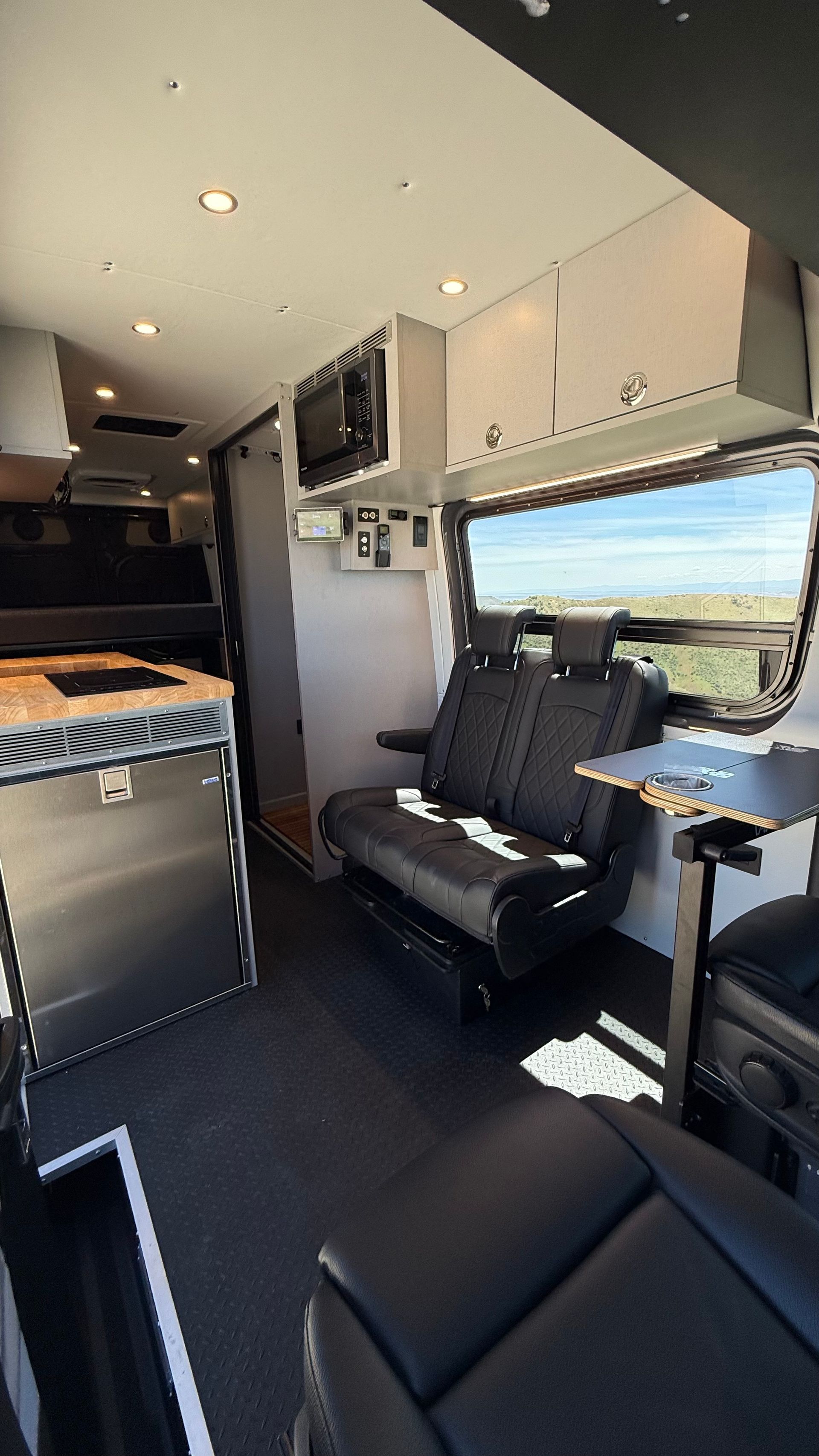 Compact camper van interior with bench seat, cabinet storage, and large side window overlooking a landscape