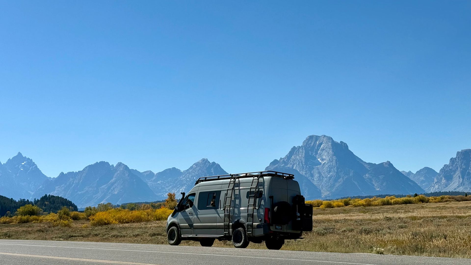 Camper van parked on a roadside in a mountain landscape under a clear blue sky.