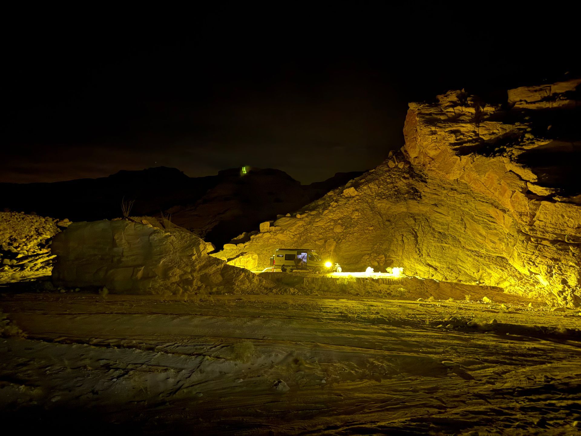 Illuminated rocky desert landscape at night with a dark sky and glowing yellow lights on a cliff face