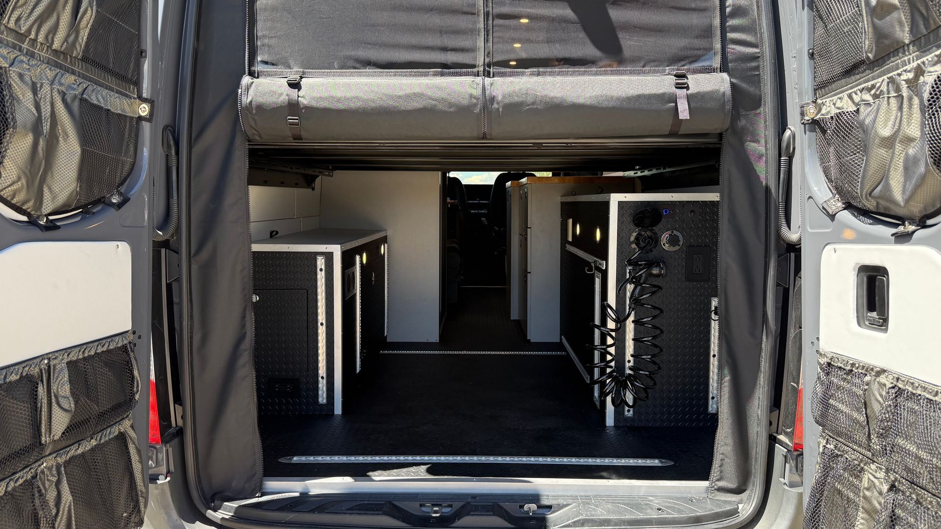 Open rear cargo area of a black camper van with a central aisle and storage cabinets