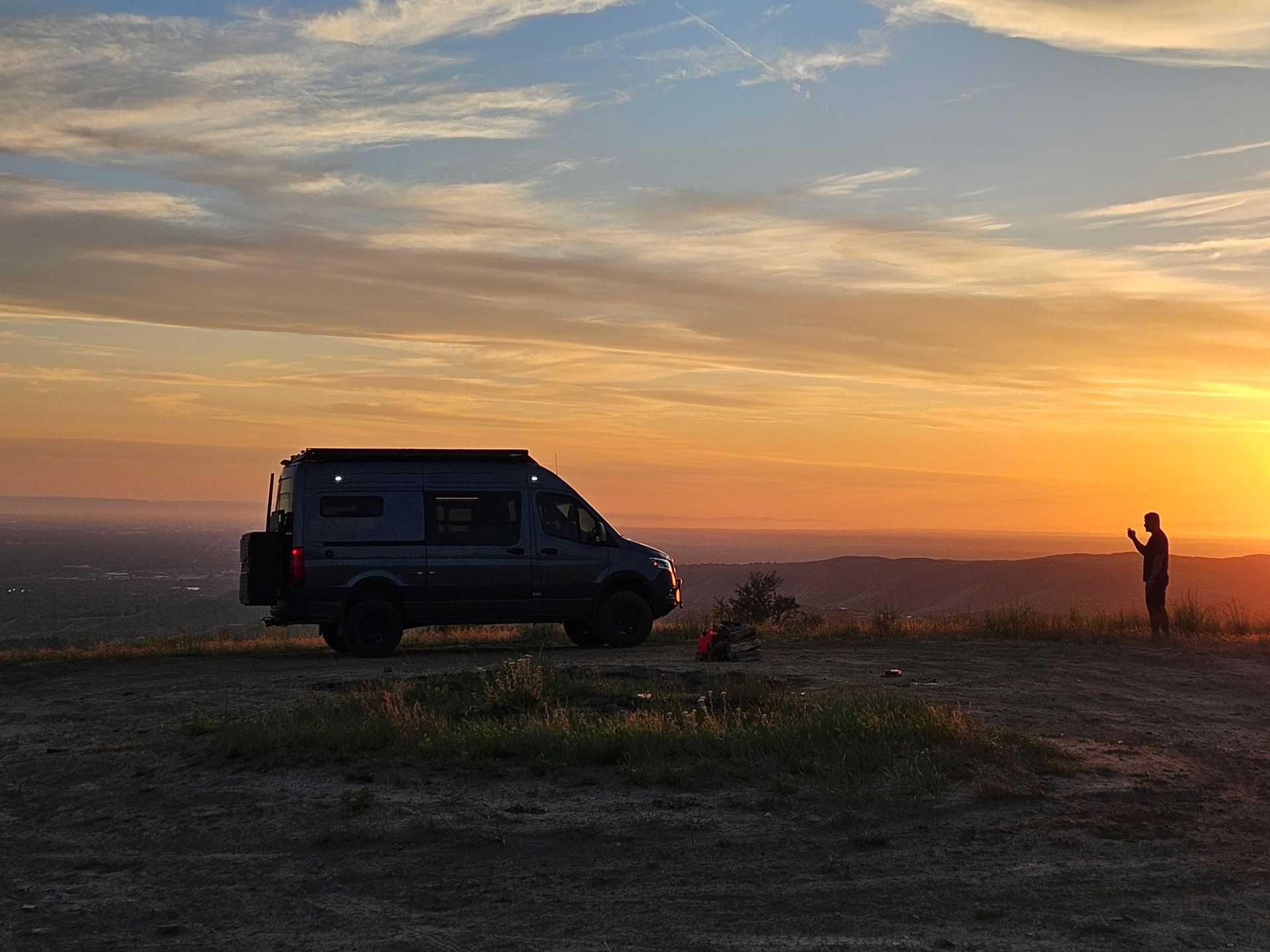 Van parked on a dusty plain at sunset, with a person standing nearby taking a photo