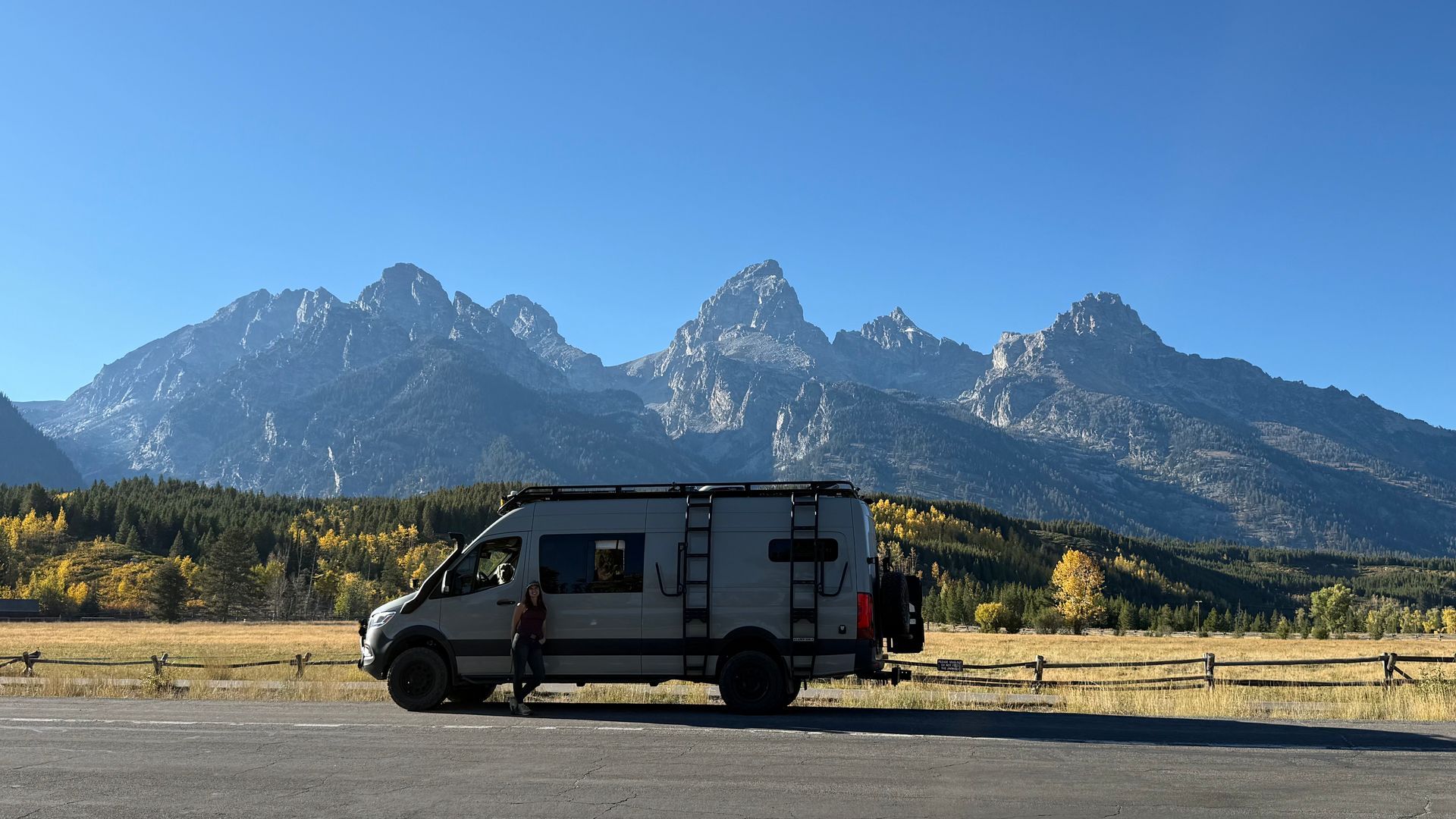 White van parked on a dirt road with mountains and autumn trees in the background.
