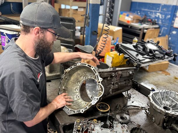 Mechanic inspecting a transmission case on a workbench in a repair shop.