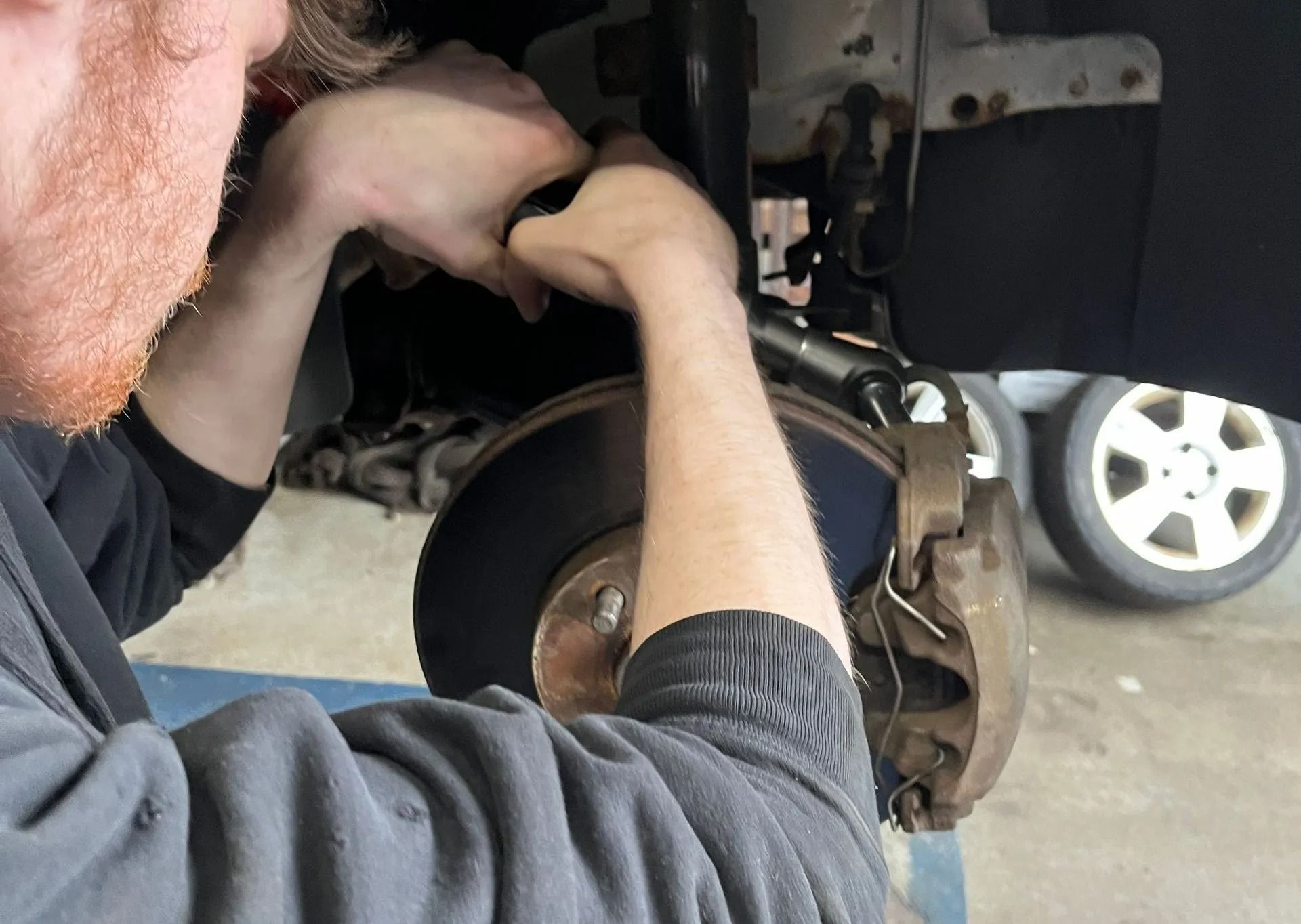 A person works on a car's brakes; they are holding a part above a brake rotor.