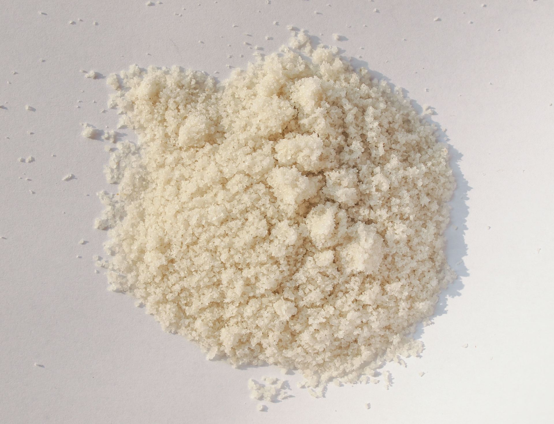 A pile of coarse, off-white, granulated powder or dry food crumbs centered on a plain white background.