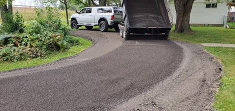 A dump truck distributes gravel onto a curved driveway in a residential yard.