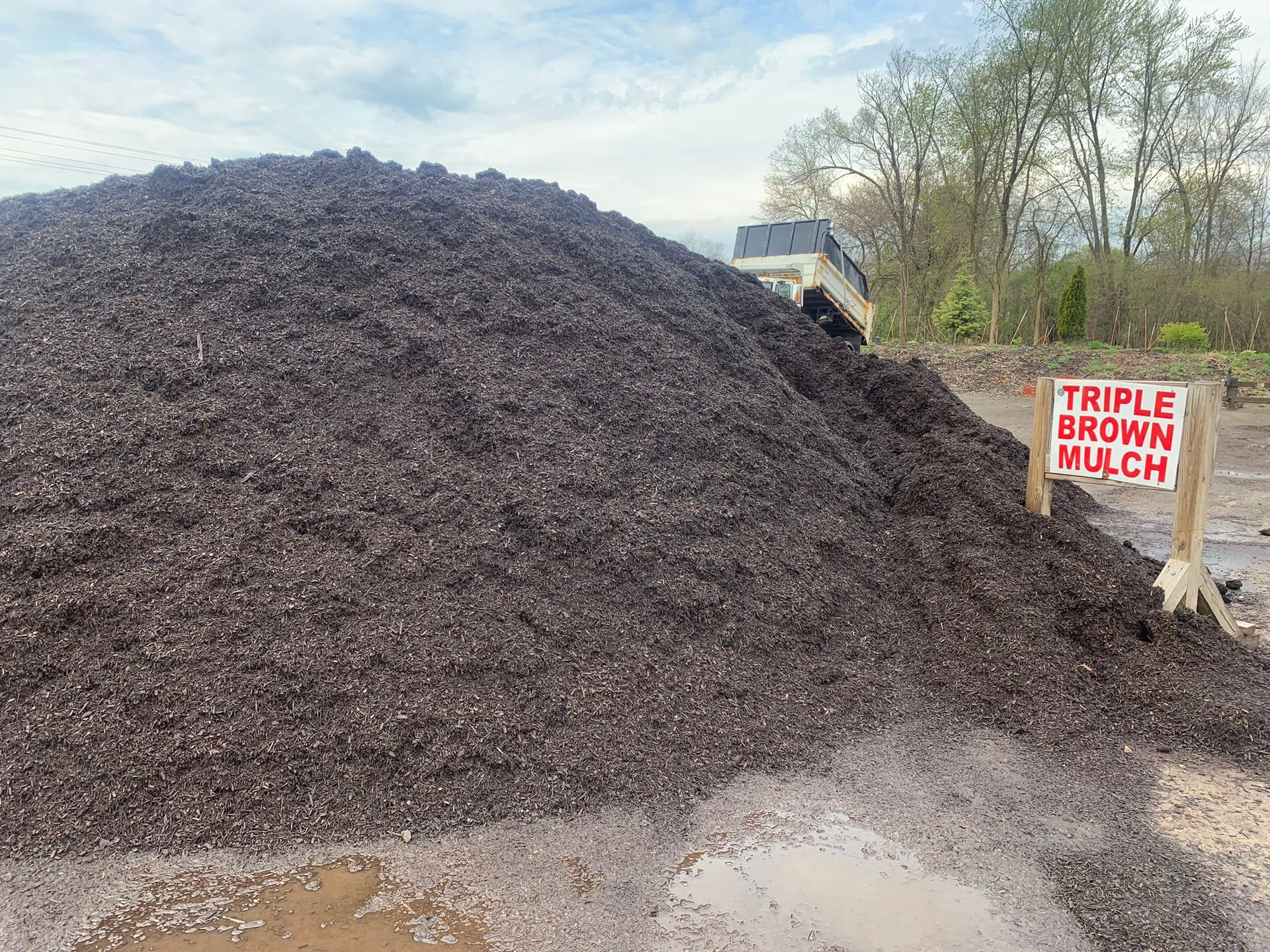 A large pile of dark brown mulch with a sign next to it that reads, 