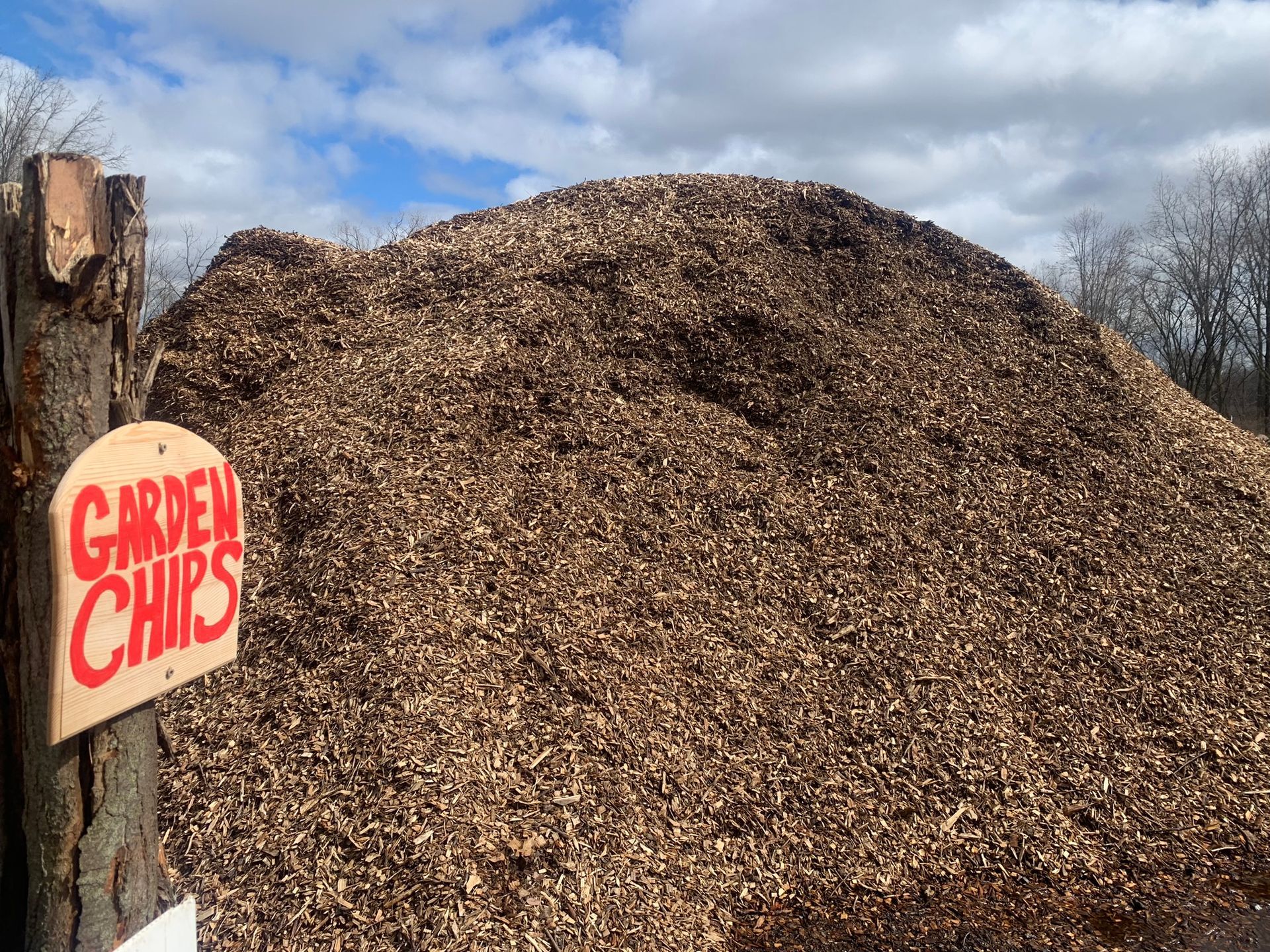A large pile of wood garden chips next to a wooden sign that reads 