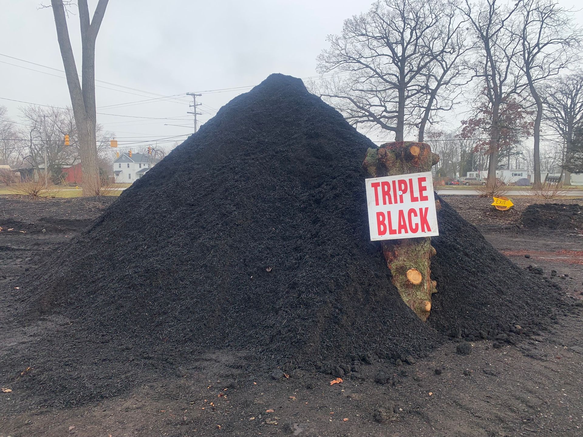 A large, conical pile of dark black mulch with a sign that reads 