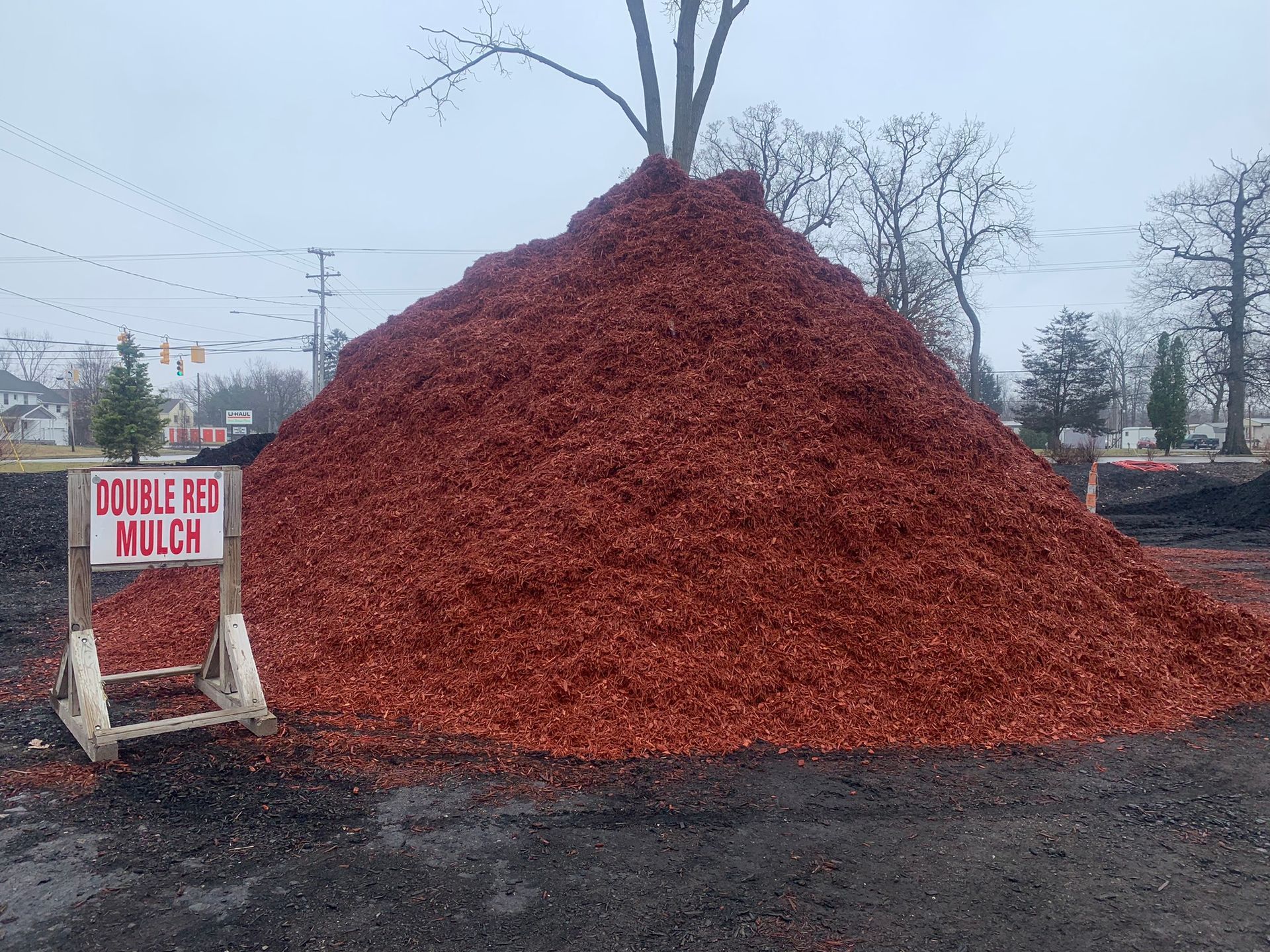 A large, conical pile of vibrant red mulch sits outdoors with a sign in front labeled 