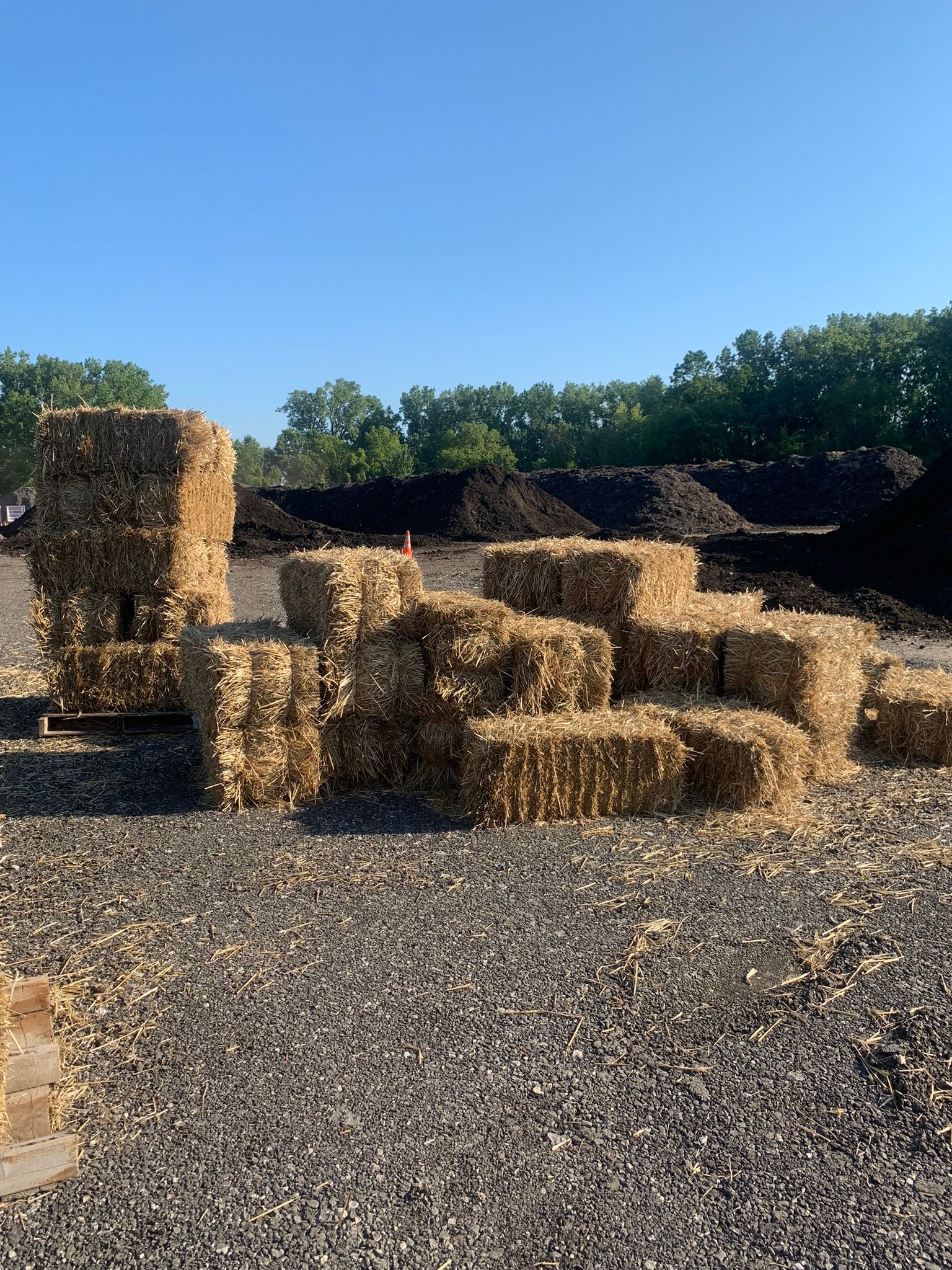 A stack of rectangular straw or hay bales sitting on a gravel surface outdoors under a clear blue sky.