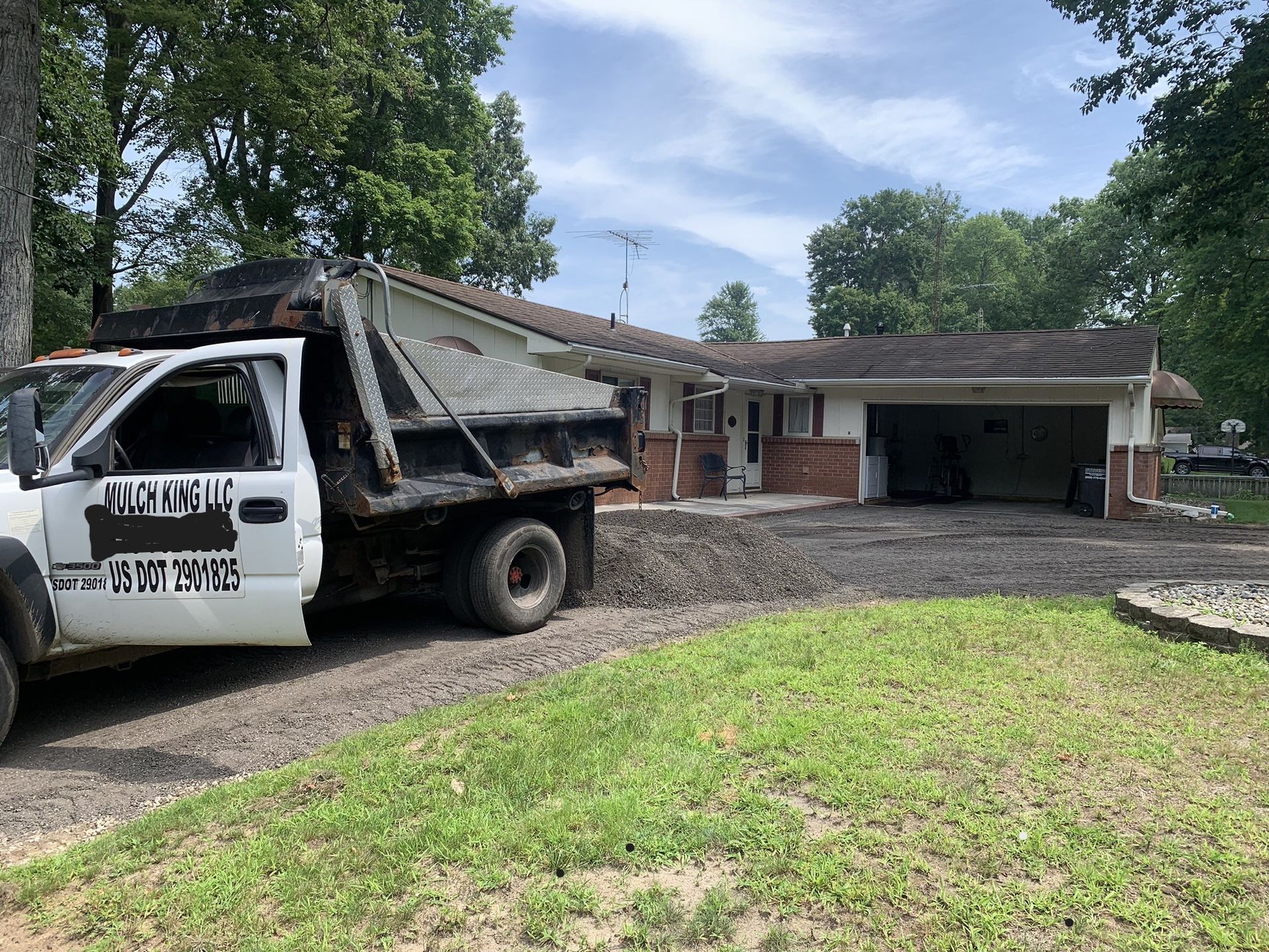 A white dump truck parked in a gravel driveway in front of a residential house with a garage.