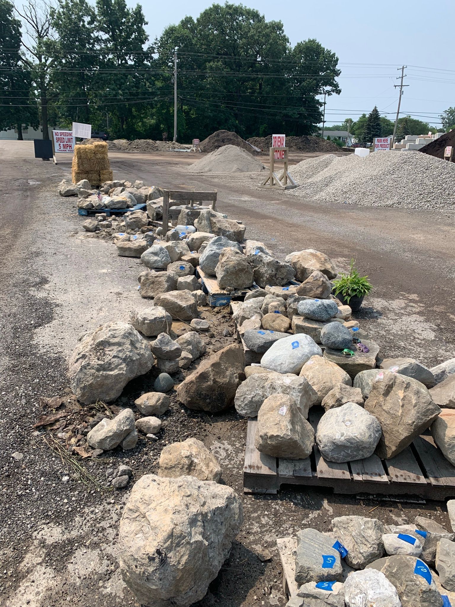 An outdoor landscape supply yard displays various large rocks and boulders arranged on wooden pallets on a gravel lot.