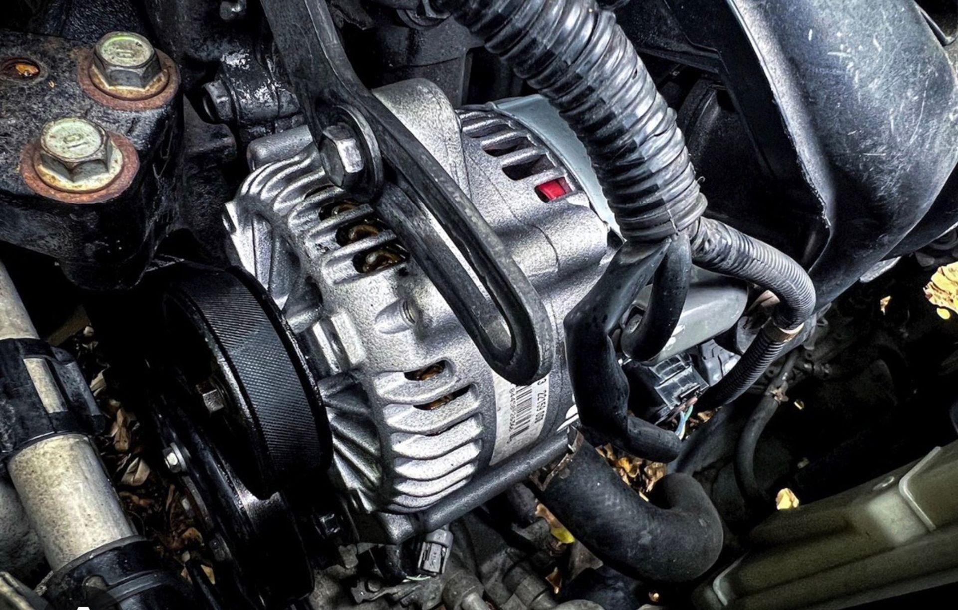 Close-up of a car engine bay with a silver alternator and black belts and hoses