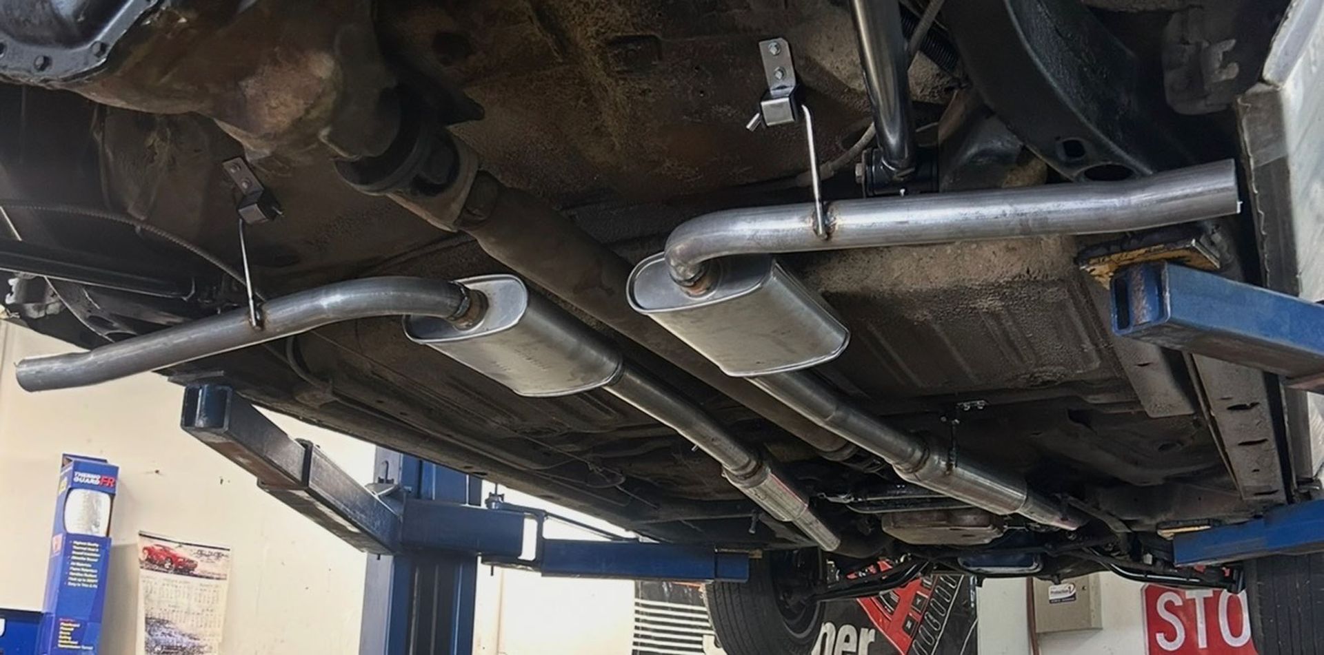 The undercarriage of a vehicle on a lift, showing a dual exhaust system with mufflers and steel pipes.